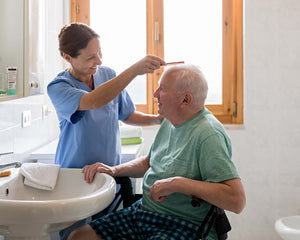 Elderly man having his hair brushed by carer