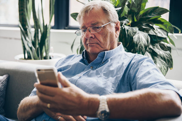 Man sitting on a couch using a smartphone with plants in the background