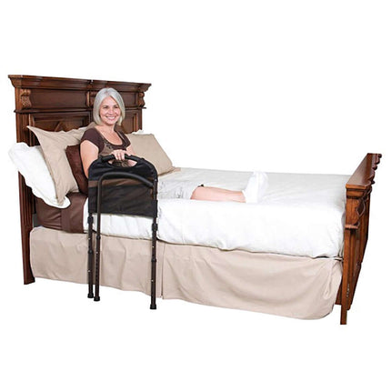 A smiling woman using the Stander Mobility Bed Rail for support while sitting on a bed.
