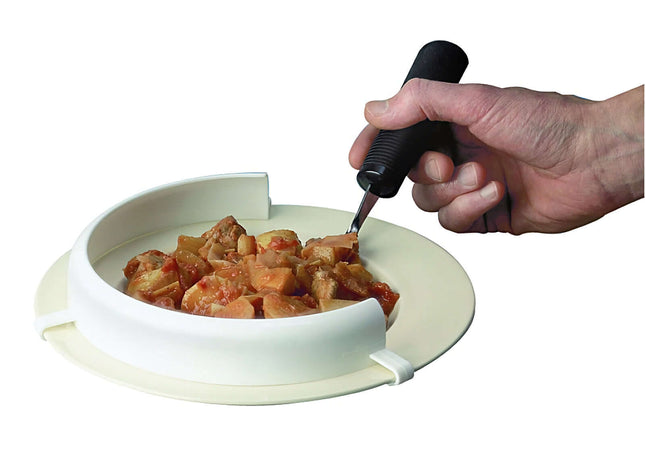 Flexible Food Guard attached to a plate aiding one-handed eating, with a hand holding a utensil, preventing food spillage.