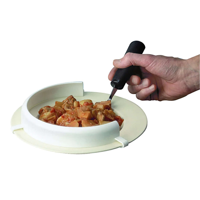Flexible white food guard attached to a plate, assisting one-handed eating with food collection.